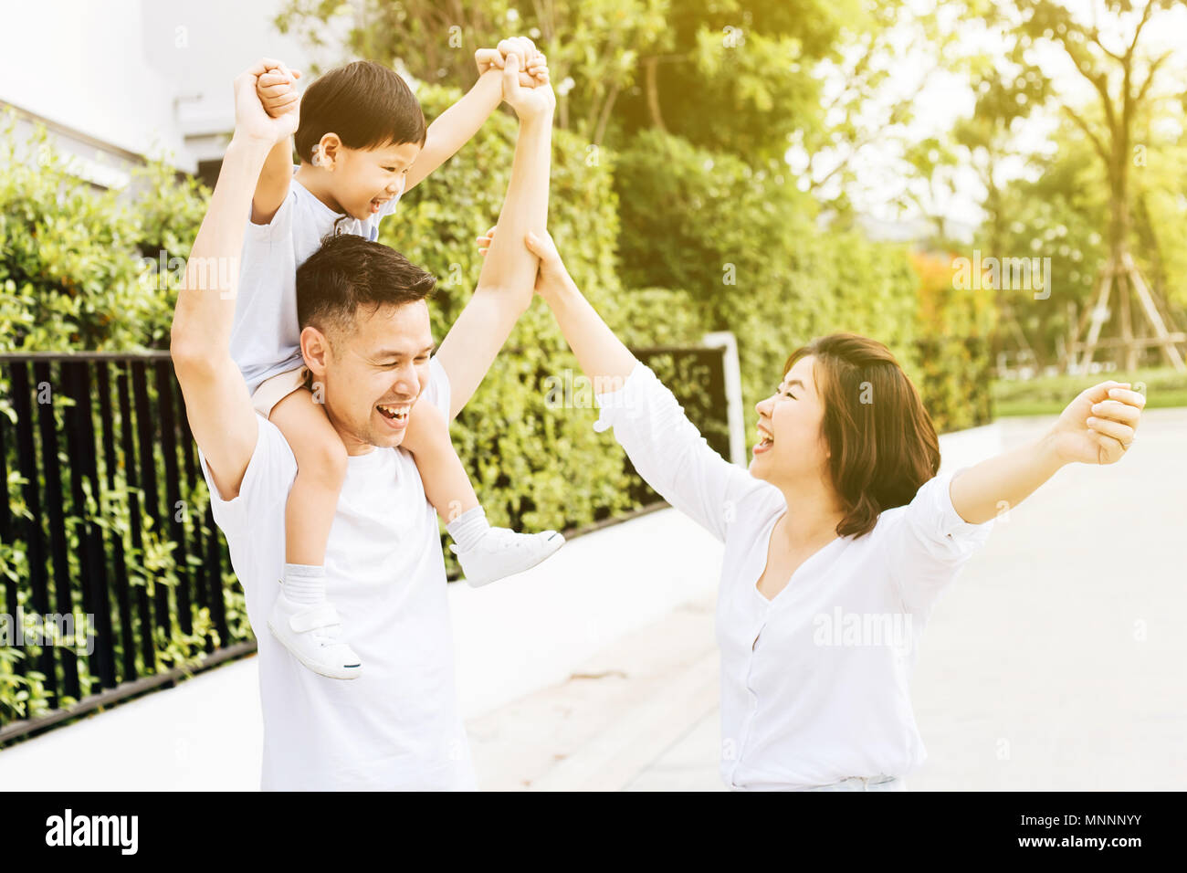 Carino padre asiatici piggy backing suo figlio insieme con sua moglie nel parco. Famiglia eccitato alzando le mani insieme con la felicità Foto Stock