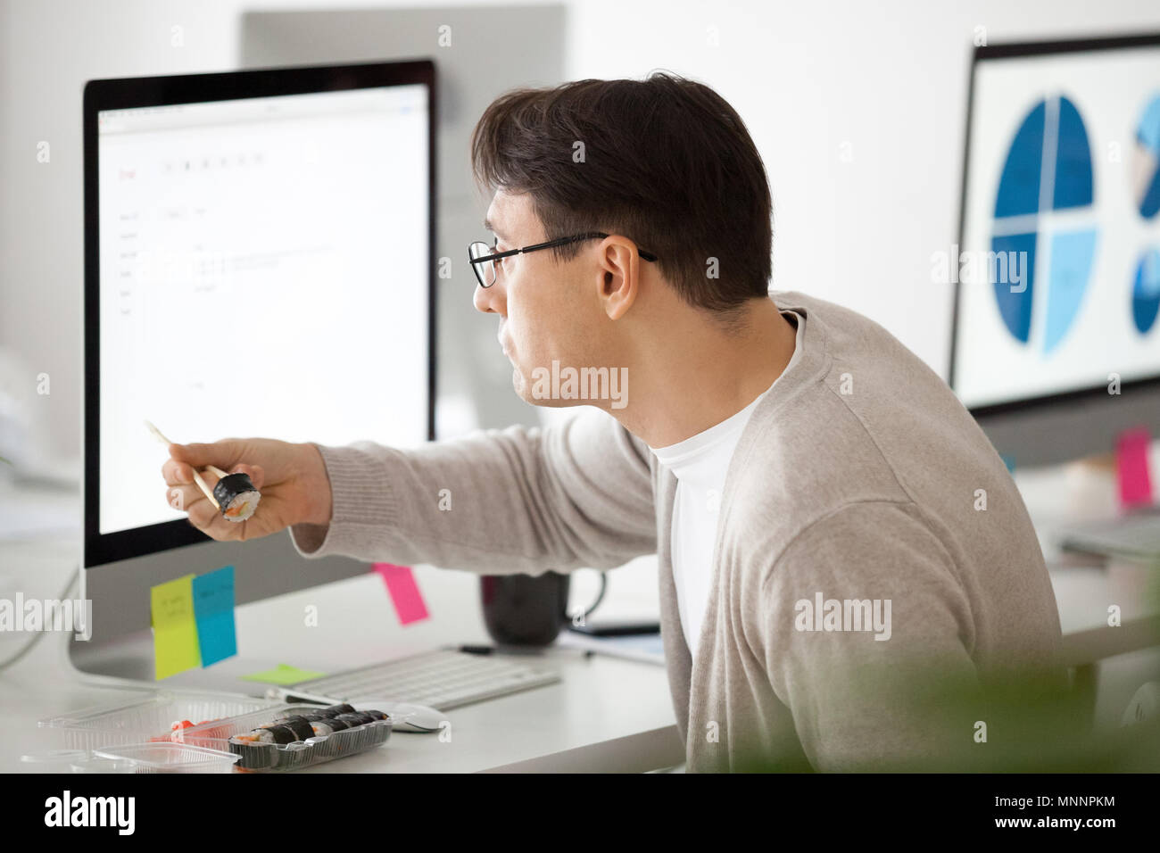 Ufficio maschio dipendente mangiare sushi roll presso il luogo di lavoro con compute Foto Stock