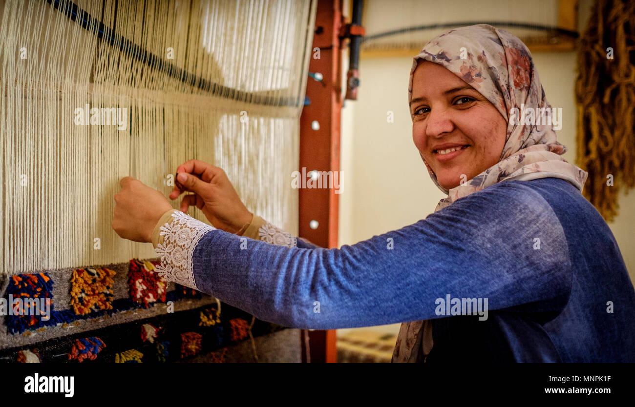 Una donna in abito tradizionale si siede la tessitura dei tappeti in Tazenakht, sud del Marocco, Africa Foto Stock