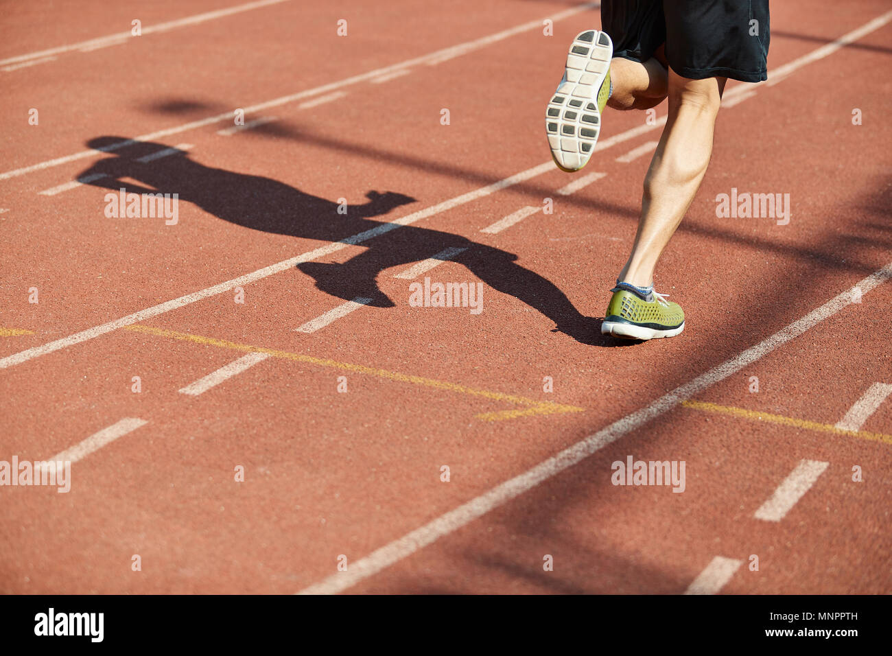 Gambe e ombra di un maschio di atleta che corre sulla pista. Foto Stock