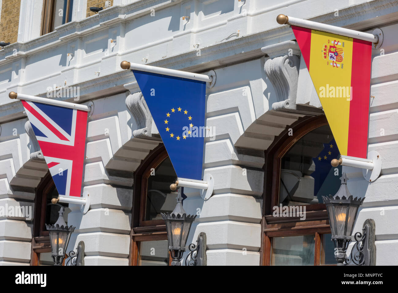 Spagnolo e britannico e bandiere europee tutti volare insieme al di fuori di un grande classico edificio progettato con archi. pennoni e gli emblemi europea. Foto Stock