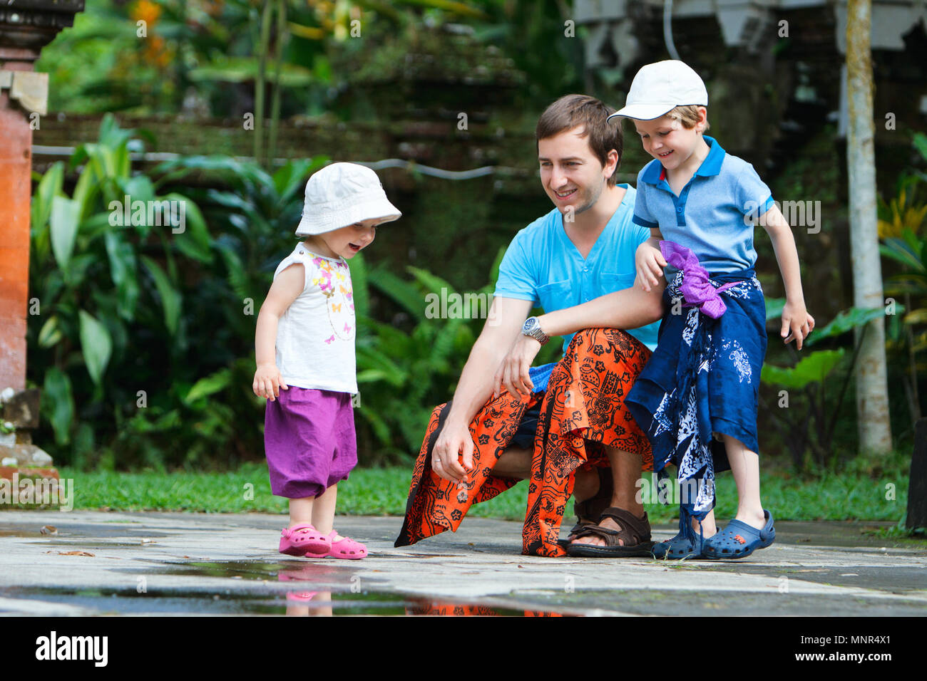 Padre e i suoi due bambini che indossano sarong visitando il Tempio di Bali Foto Stock