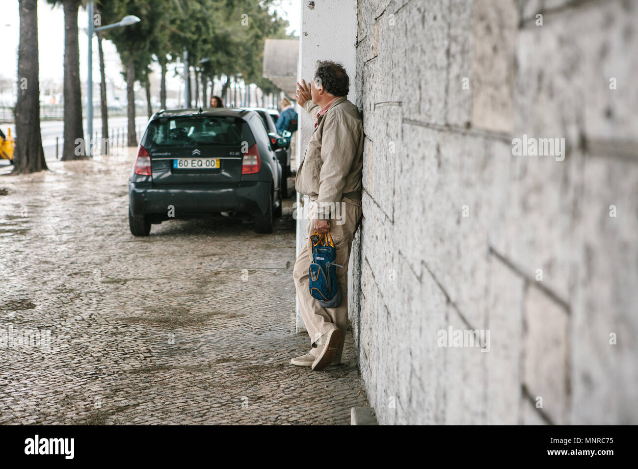 Lisbona, Portogallo 01 maggio 2018: uomo vicino a parete sul marciapiede attende. Pedone o turistico a street e di attesa o riposo o a piedi. Foto Stock