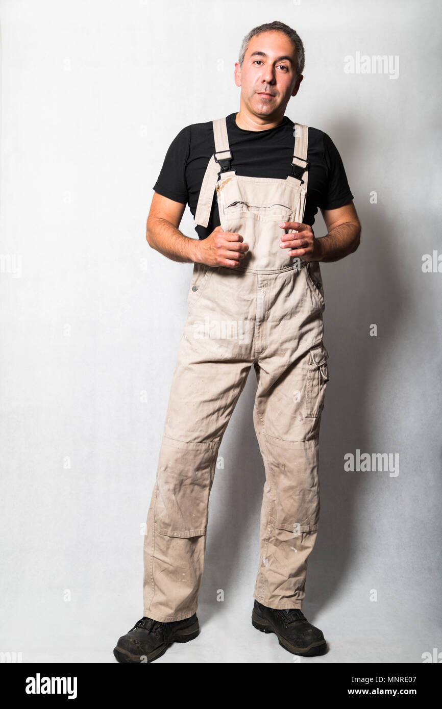 Uomo maschio collaboratore specializzato idraulico, ingegnere o costruttore  in bianco sporco vecchio malandato tuta di lavoro, t-shirt nera e stivali  con le mani sulla tuta standin Foto stock - Alamy