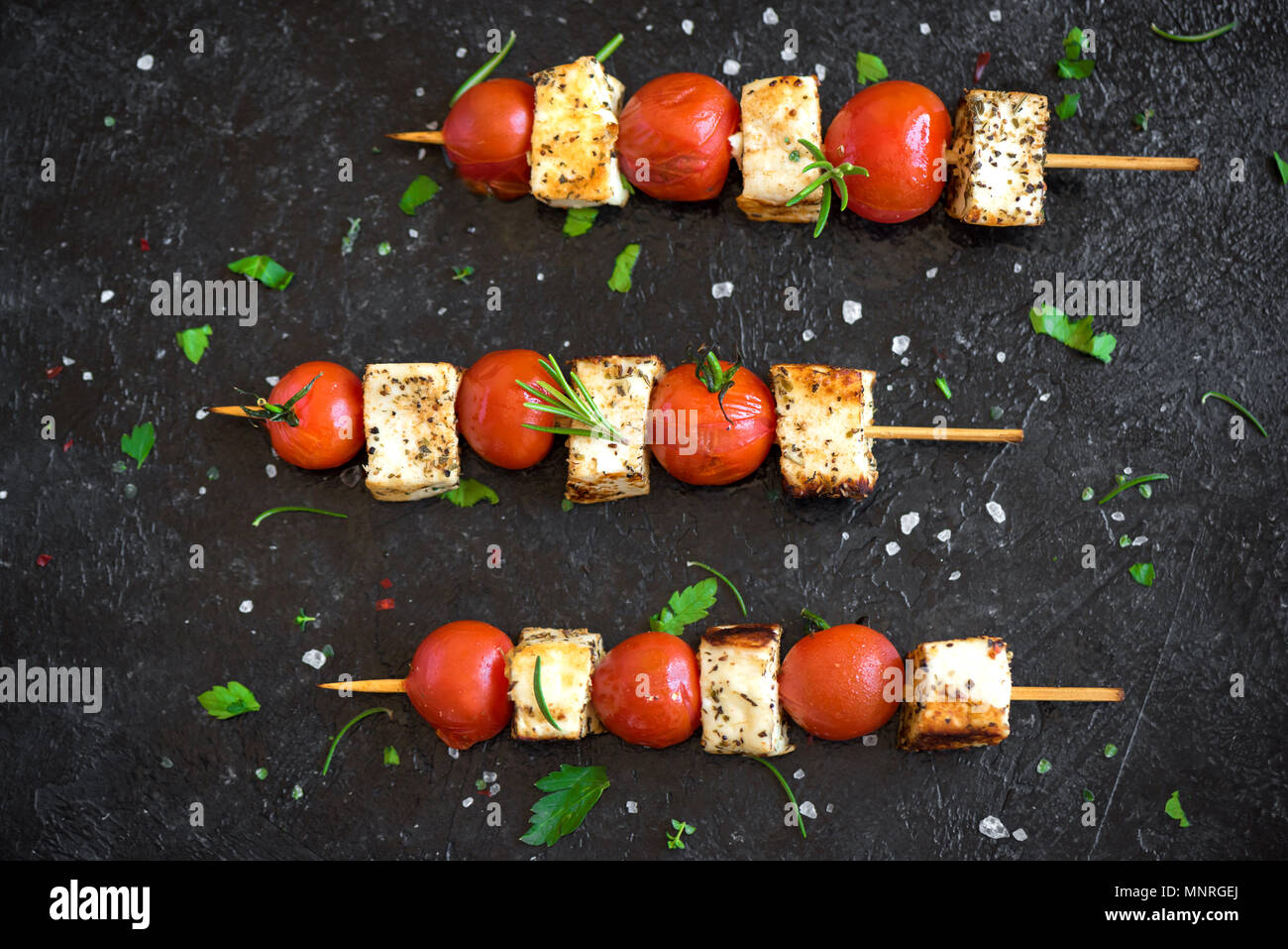 Grill vegetariano. Spiedini vegetariani con il formaggio halloumi e pomodori su sfondo nero. Foto Stock