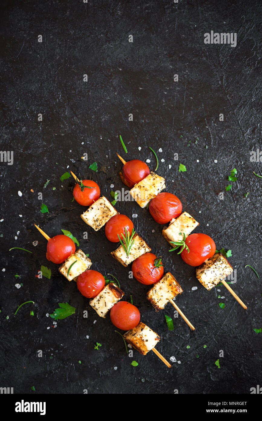 Grill vegetariano. Spiedini vegetariani con il formaggio halloumi e pomodori su sfondo nero, copia dello spazio. Foto Stock