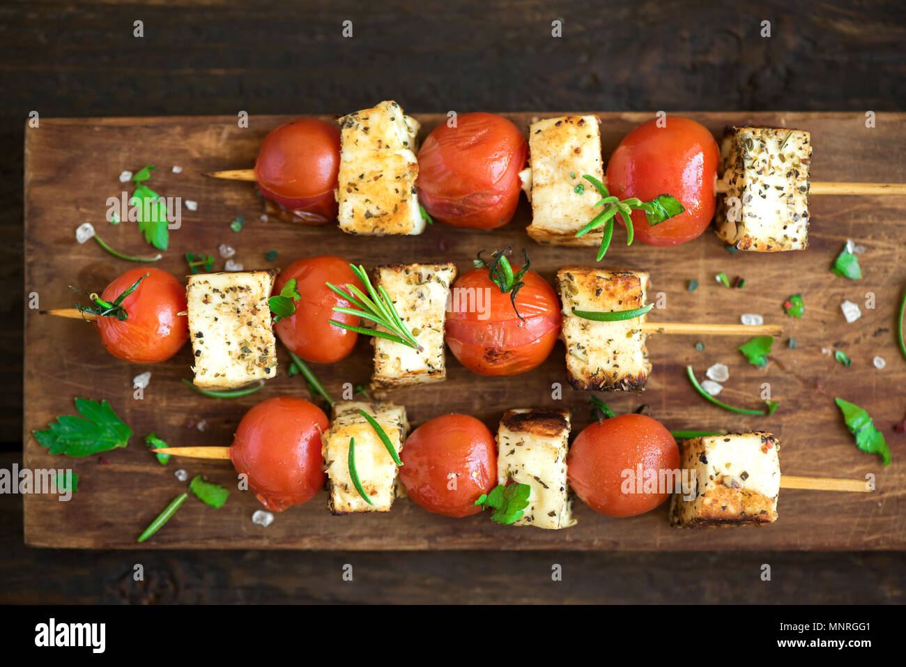 Grill vegetariano. Spiedini vegetariani con il formaggio halloumi e pomodori su sfondo di legno. Foto Stock