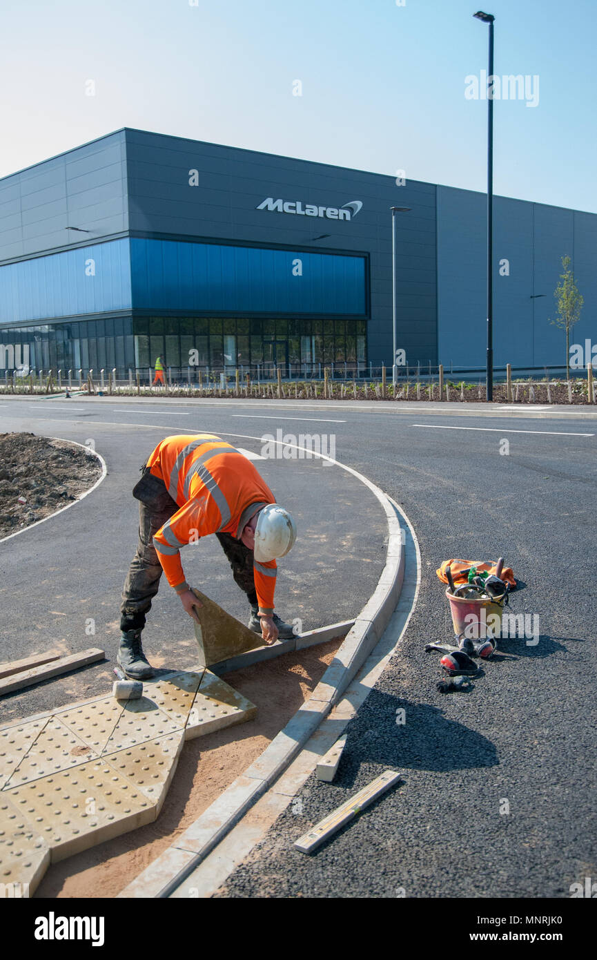 Operaio edile che posa pavimentazione tattile vicino all'edificio del gruppo McLaren, Woking, Regno Unito, in una giornata luminosa. L'industria moderna incontra le infrastrutture pubbliche Foto Stock