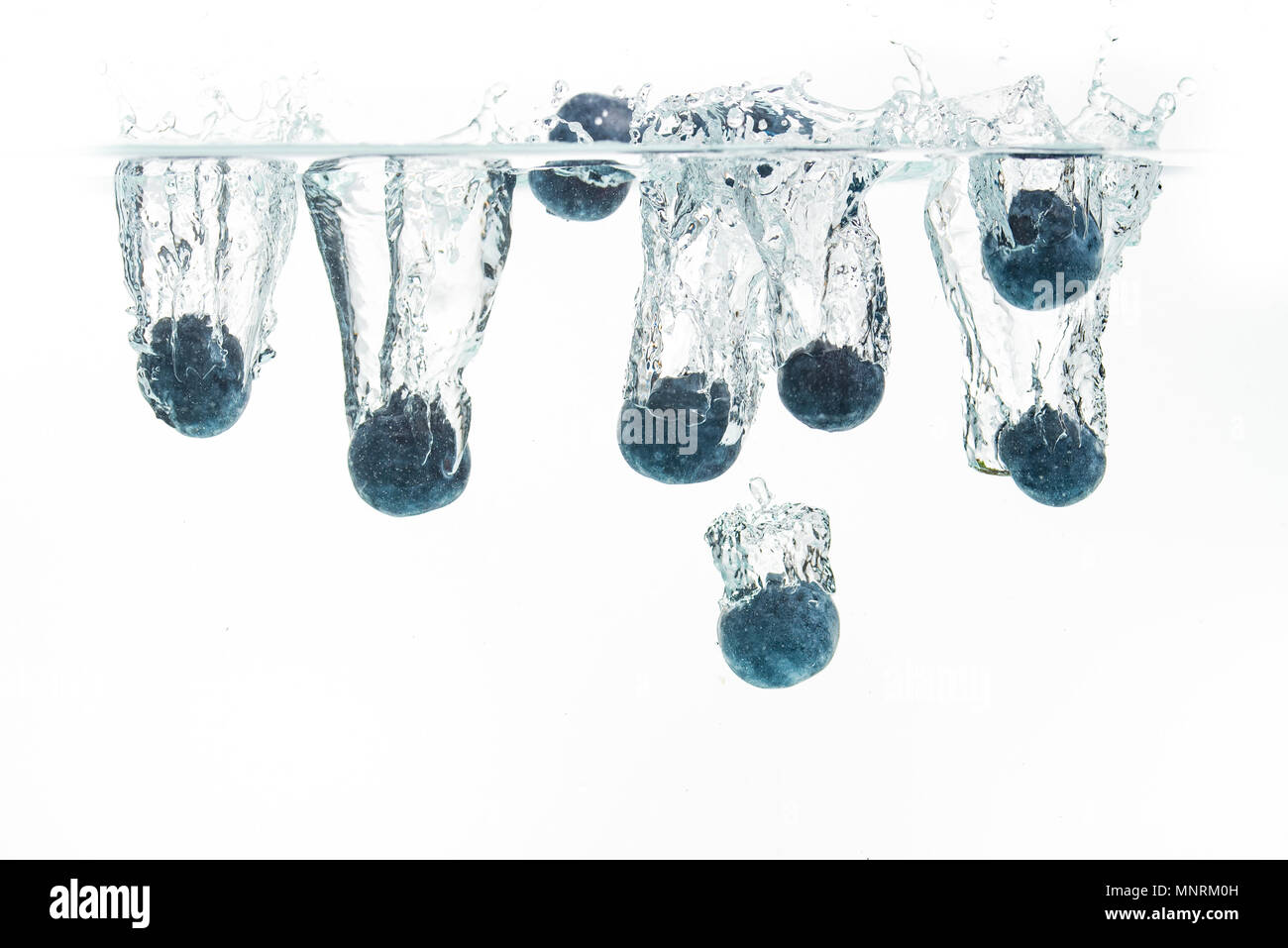 I mirtilli che affonda nell'acqua con bolle di aria sullo sfondo bianco Foto Stock