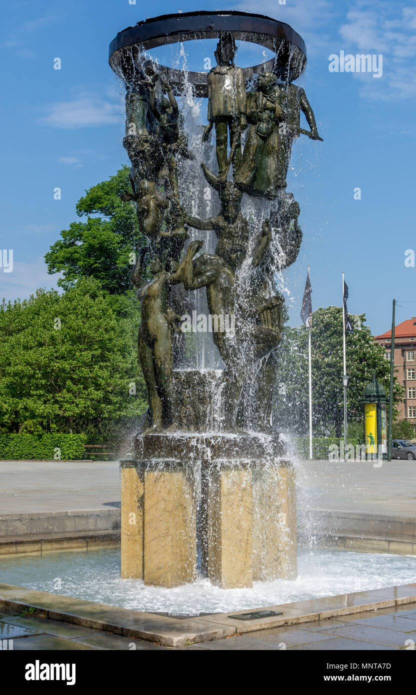 Fontana costruita di statue in bronzo di persone in piedi sulle spalle dell'altra con acqua che cade su un plinto in cemento. Foto Stock