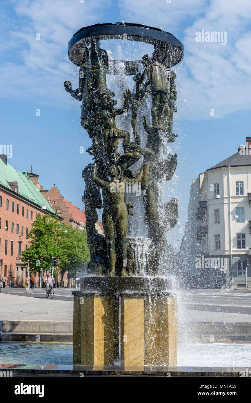Fontana costruita di statue in bronzo di persone in piedi sulle spalle dell'altra con acqua che cade su un plinto in cemento. Foto Stock