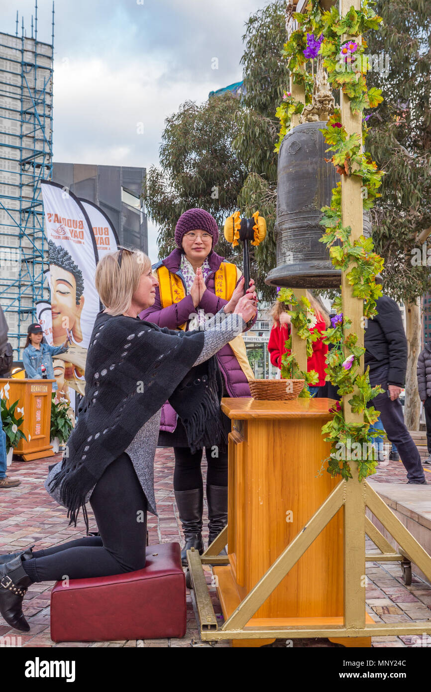 Profilo di shot dai capelli biondi donna inginocchiato sulla pelle di colore rosso kneeler colpendo le grandi campana ottone giallo con un mazzuolo mentre attendant orologi. Foto Stock