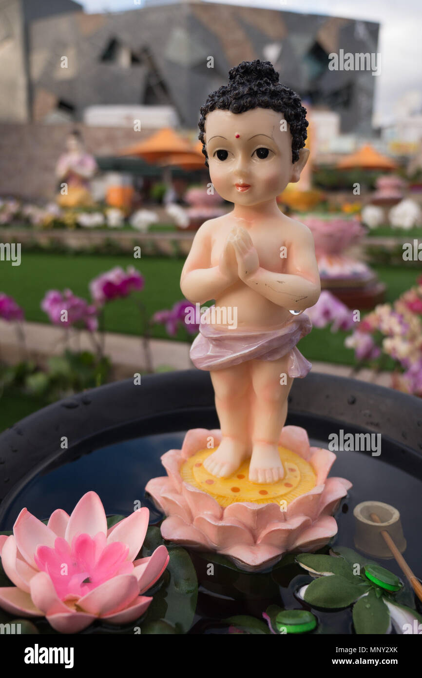 Di plastica e piccoli Buddha bambino con i capelli neri grandi occhi e mani giunte in piedi su un colorato lotus in un piccolo recipiente di acqua di rosa e verde lotus. Foto Stock