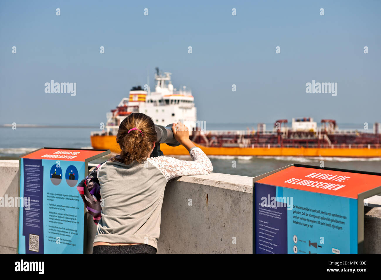 Giovane ragazza guarda attraverso un binocolo ad le navi che passano sulla Schelda occidentale vicino al porto olandese città di Terneuzen Foto Stock