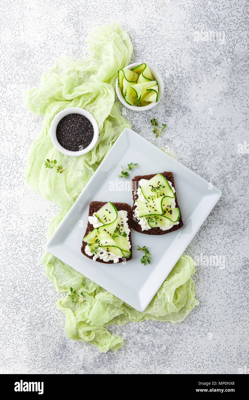 Crostini di pane di segale con ricotta, cetriolo e sesamo nero su grigio ardesia e pietra o calcestruzzo sfondo. Foto Stock