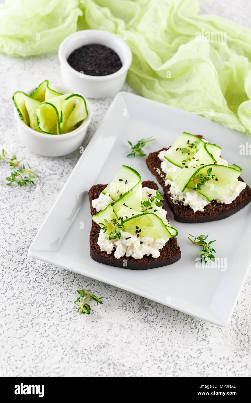 Crostini di pane di segale con ricotta, cetriolo e sesamo nero su grigio ardesia e pietra o calcestruzzo sfondo. Foto Stock