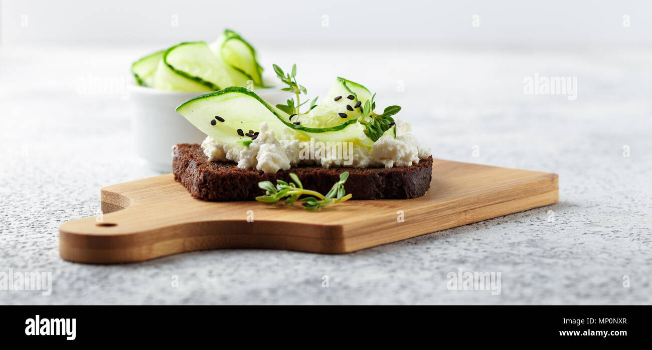 Crostini di pane di segale con ricotta, cetriolo e sesamo nero su grigio ardesia e pietra o calcestruzzo sfondo. Foto Stock