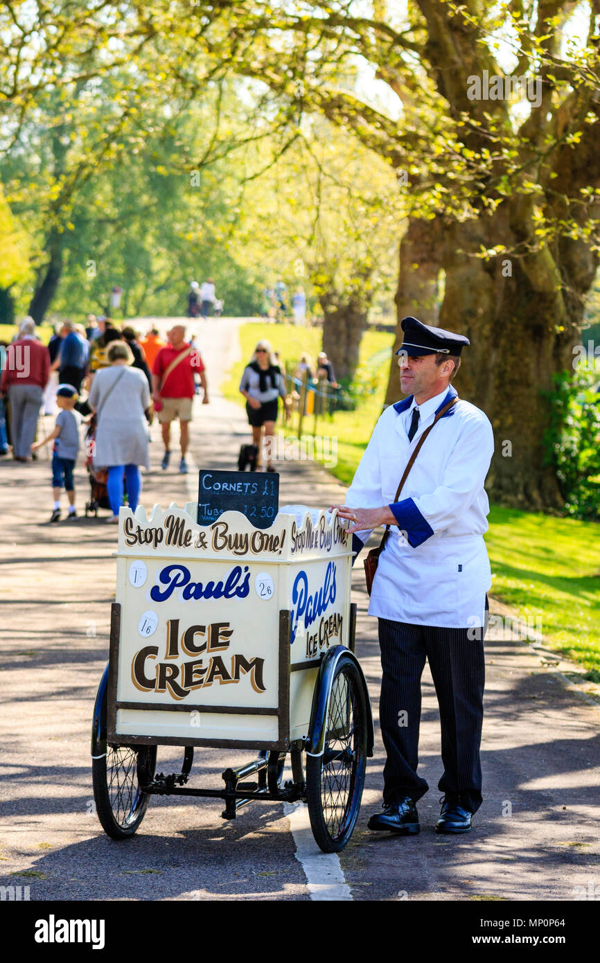 Saluto alla 40s manifestazione popolare in Inghilterra. Inglese circa 1940s gelato venditore con carrello a mano sul sentiero sotto gli alberi. Foto Stock