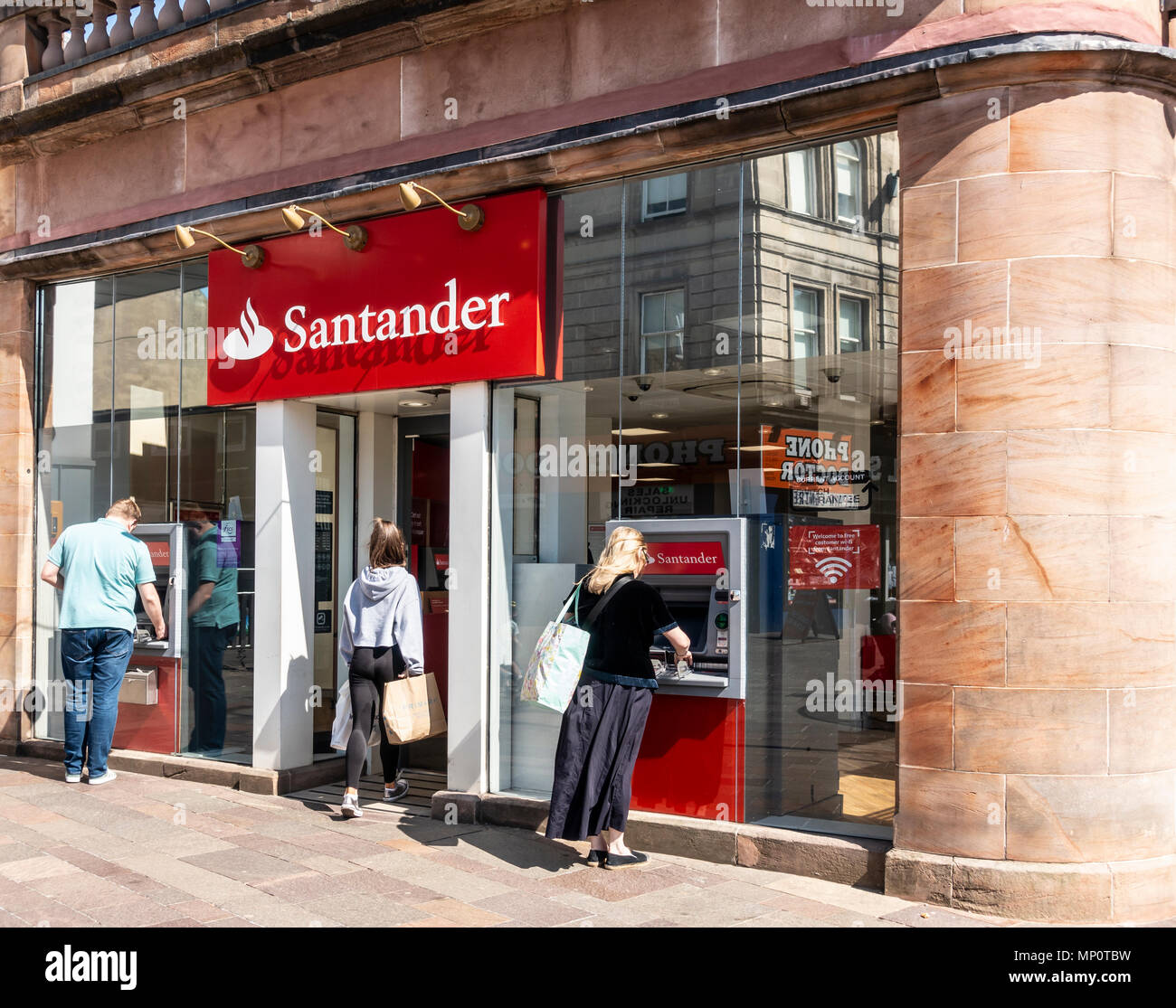 Un cliente entra in una filiale della banca di Santander mentre due altri utilizzano gli sportelli bancomat all'esterno. Hamilton, South Lanarkshire, Scotland, Regno Unito Foto Stock
