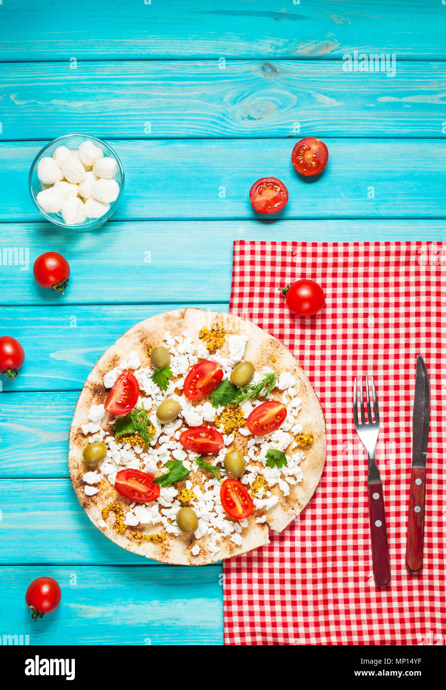 Pita con formaggio, pomodori ciliegini, olive e verde blu su sfondo di legno Foto Stock