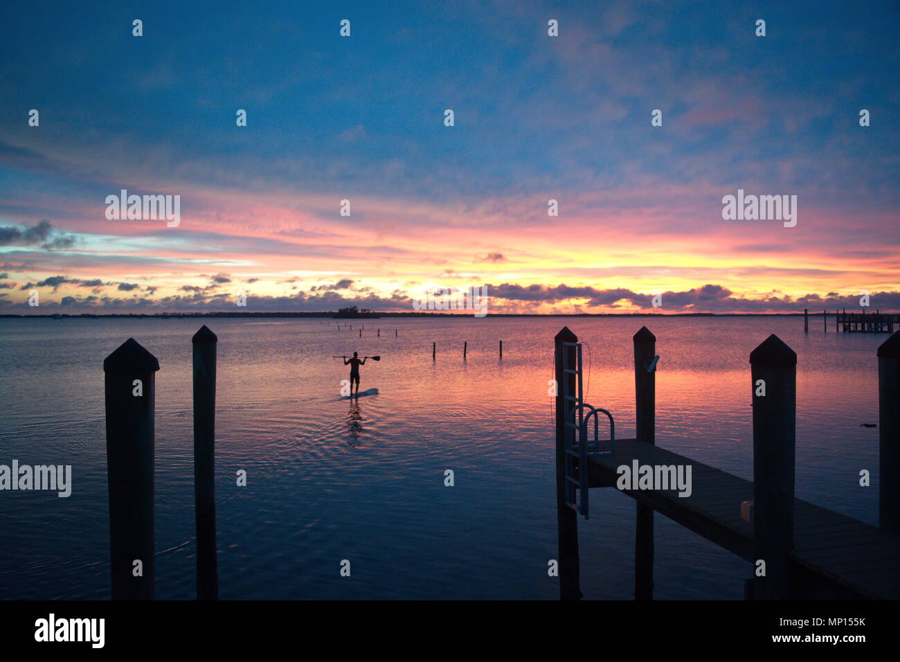Brillante tramonto colorato con le nubi sulla costa del Golfo della Florida. Uomo in piedi sulla scheda paddle, stagliano lungo i moli. Foto Stock