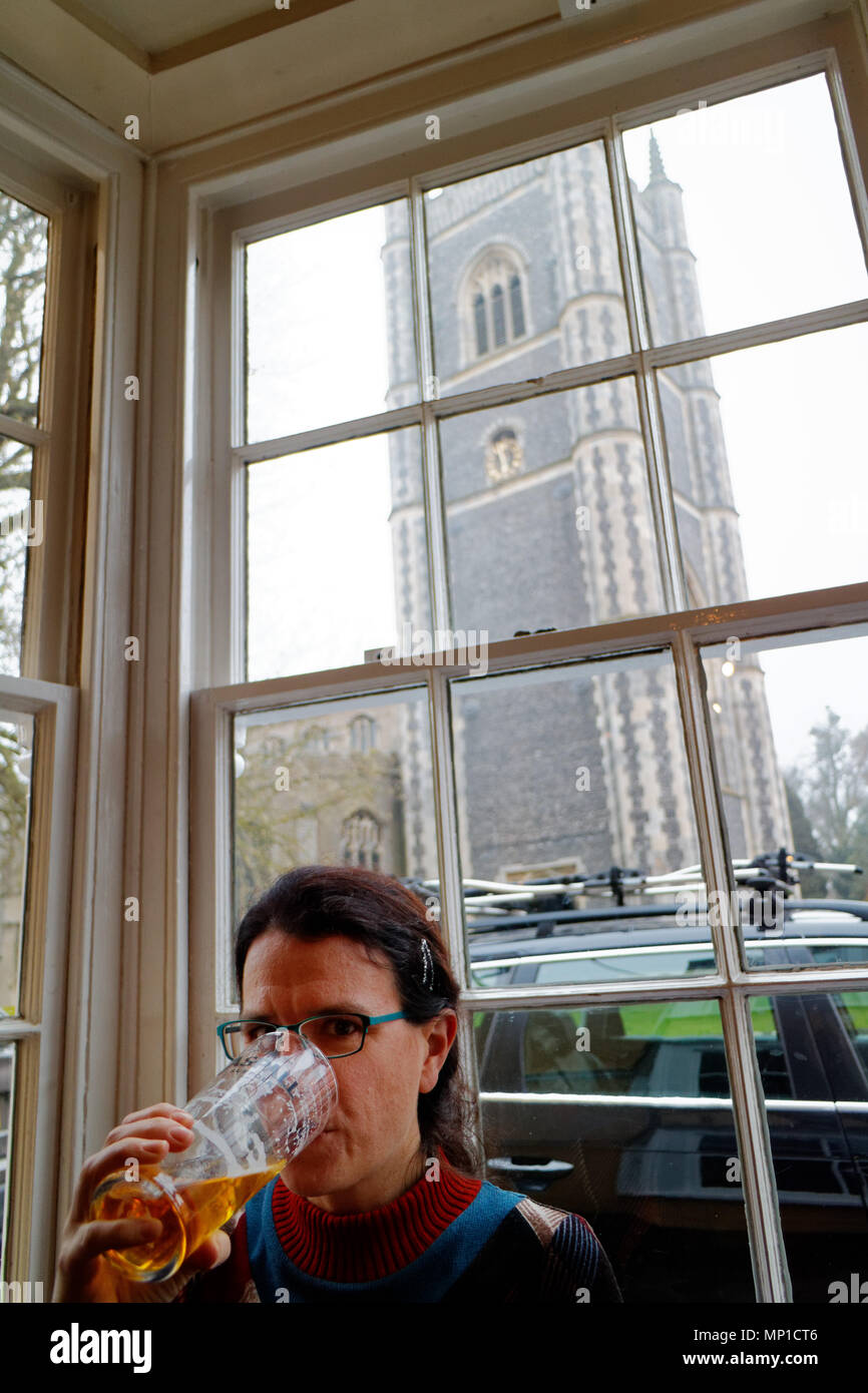 Una donna di bere una pinta in Sun Inn inDedham, con Dedham e chiesa parrocchiale visto attraverso la finestra Foto Stock