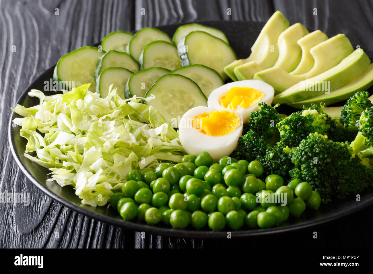 Un sano cibo verde: ortaggi freschi di avocado, piselli, cavolo, cetriolo, broccoli e uova sode close-up su una piastra orizzontale. Foto Stock