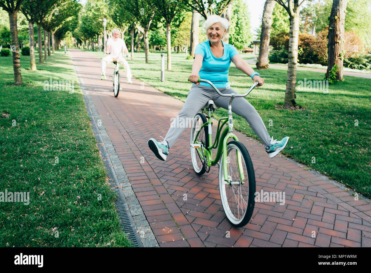 Felice coppia senior la bicicletta sul parco, funny sollevando le loro gambe fino Foto Stock