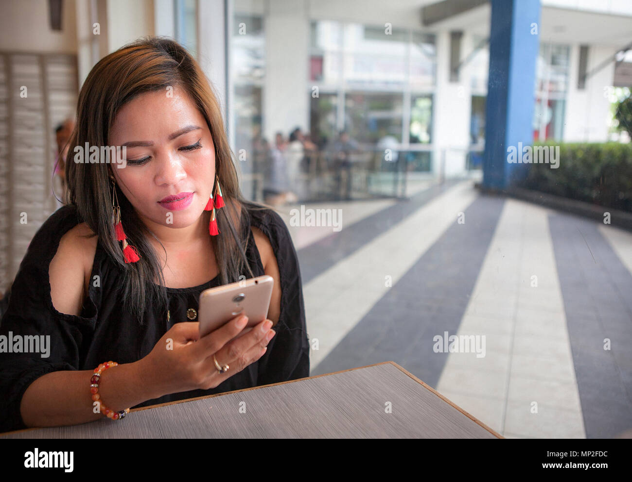 Giovane, attraente donna asiatica nelle Filippine guardando il suo smartphone in ambienti chiusi. Foto Stock