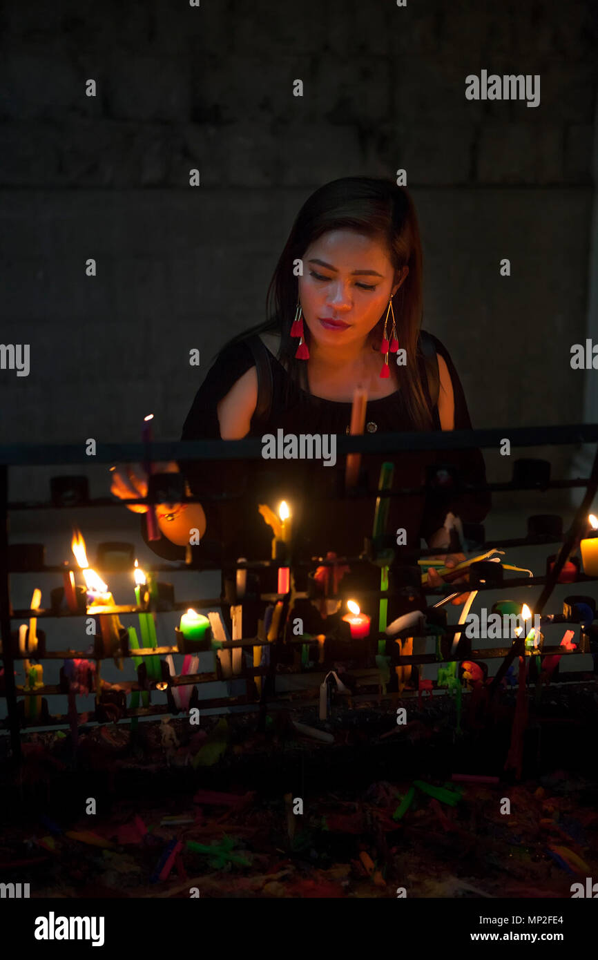 Attraente, esclusivi filippino donna asiatica luci di candele votive in una chiesa cattolica nelle Filippine. Foto Stock