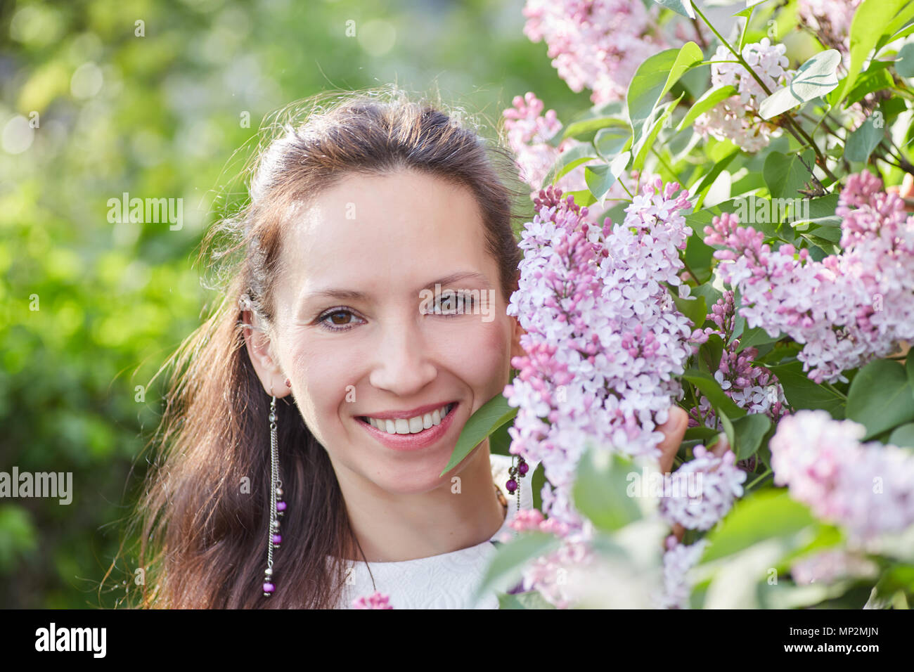 Giovane donna graziosa con bei orecchini in posa vicino al brunch di fioritura lilla Foto Stock