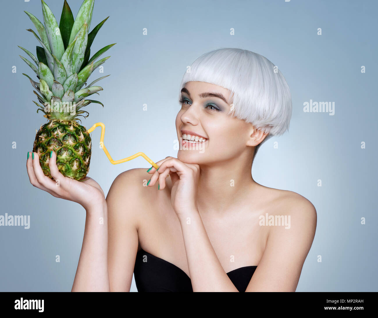 Ragazza giovane e carina con ananas cocktail. Foto di moda ragazza bionda su sfondo blu. Detox concept Foto Stock