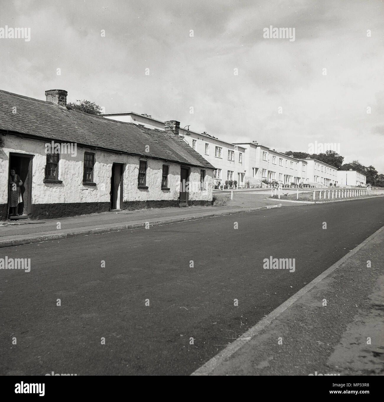 Anni '50, quadro storico, che mostra una fila di tradizionali lavoratori in pietra costruito case a un piano e poi più in alto la strada, ma più arretrato, una fila di recente costruito 'Modern', case a due piani, Irlanda. Foto Stock