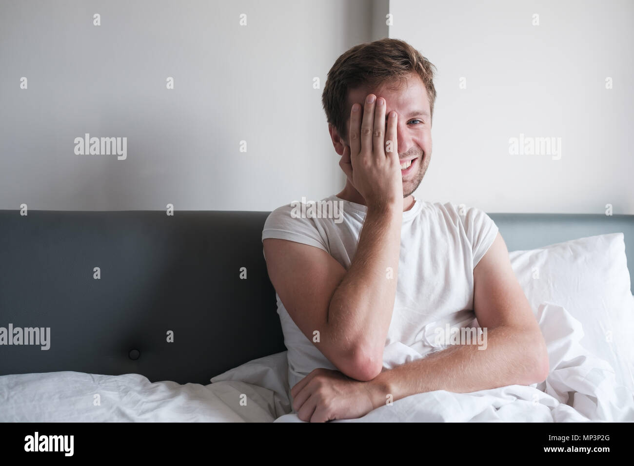 Uomo caucasico seduta a letto la mattina presto, egli è felice e sorriso chiudendo il suo volto. Foto Stock