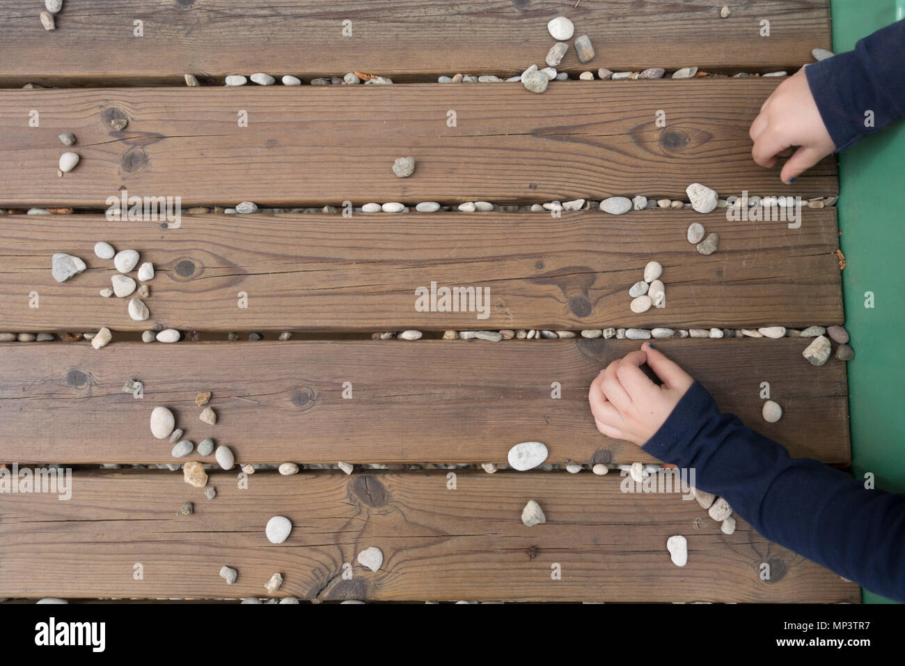 Vista superiore del bambino con le mani in mano a giocare con le pietre sul banco ligneo, escursioni all'aperto presso il parco giochi, closeup, no le persone riconoscibili, nessun popolo Foto Stock