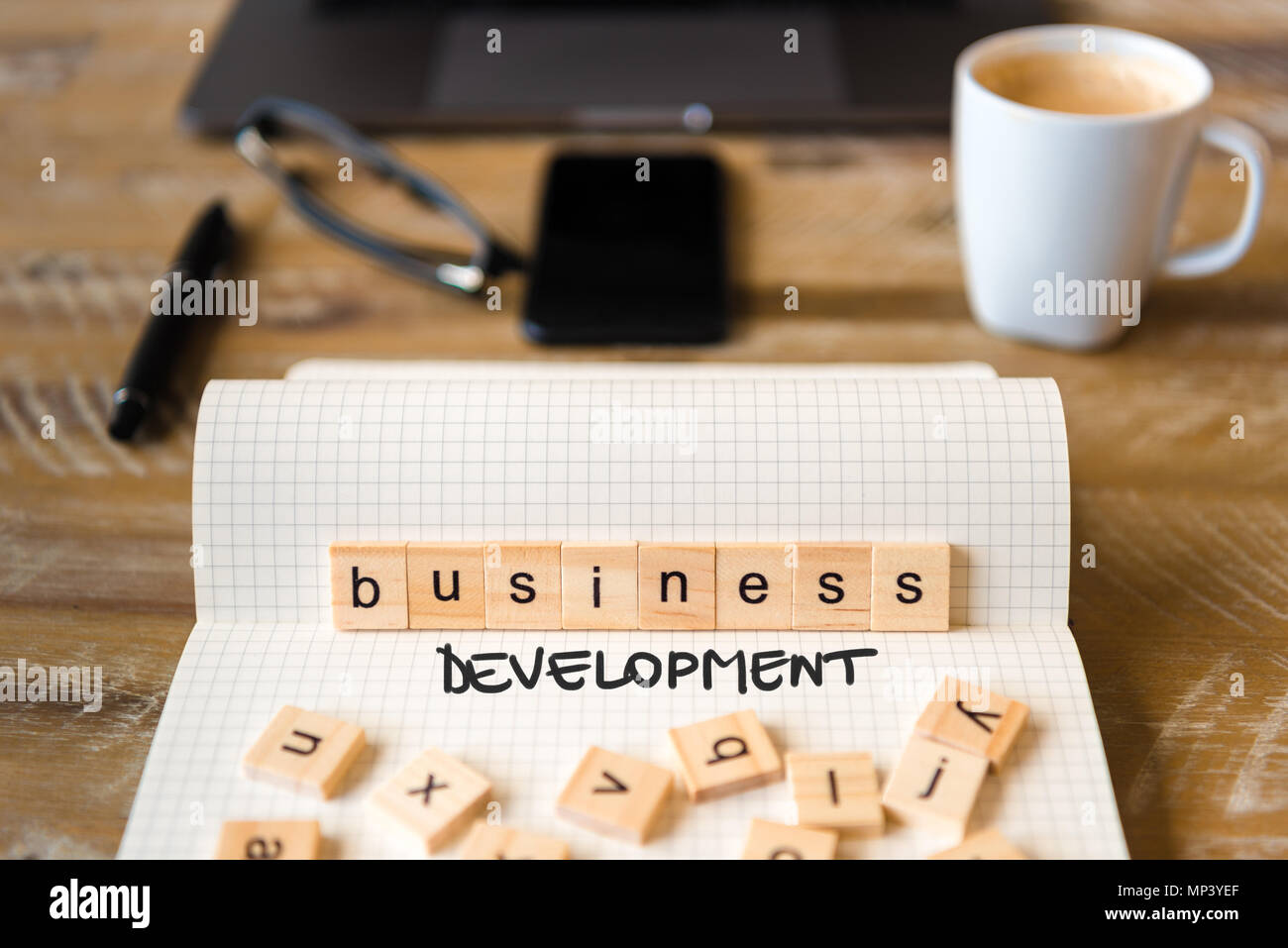 Primo piano su notebook su tavola di legno sfondo, concentrarsi sui blocchi di legno con lettere che lo sviluppo del business di testo. Foto Stock