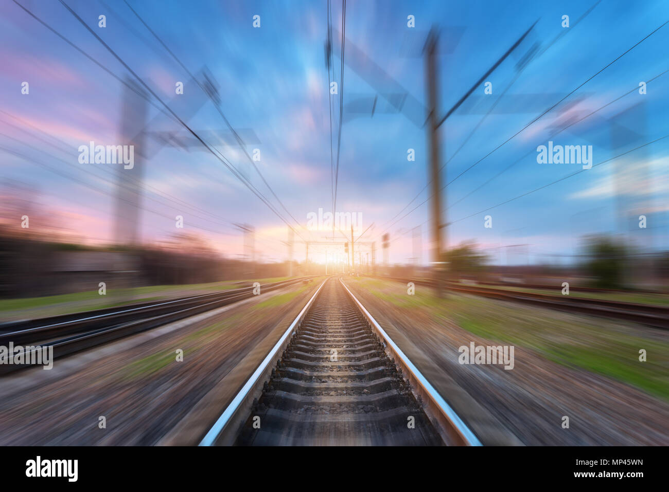 Stazione ferroviaria con motion blur effetto al tramonto. Ferrovia sfocata. Industriale paesaggio concettuale con sfocate stazione ferroviaria, blu cielo con colo Foto Stock