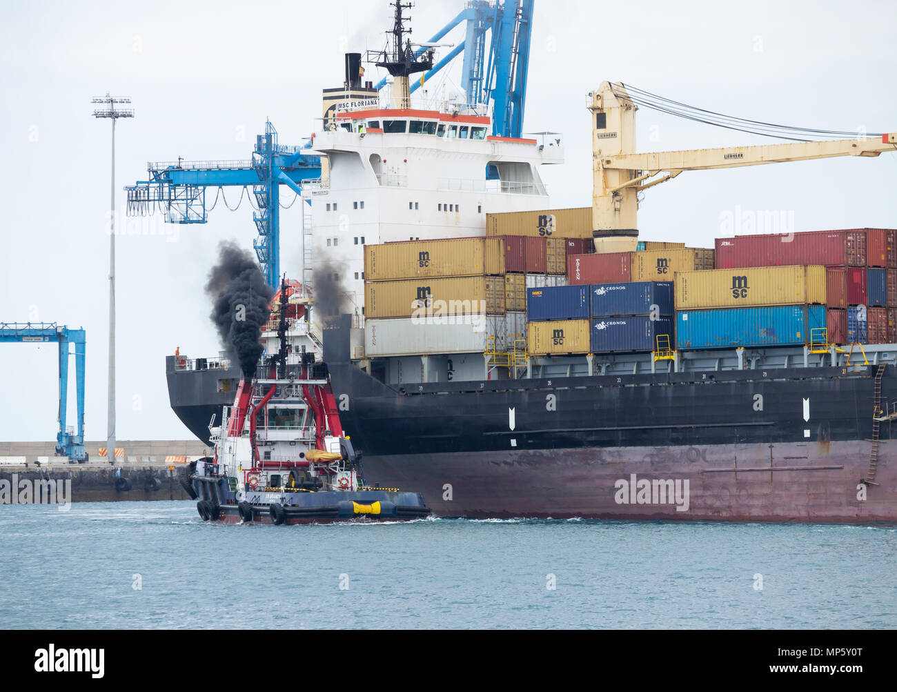 Rimorchiatore eruttazioni nero fumo come esso guide MSC Floriana nave container nel porto di Las Palmas de Gran Canaria Isole Canarie Spagna Foto Stock