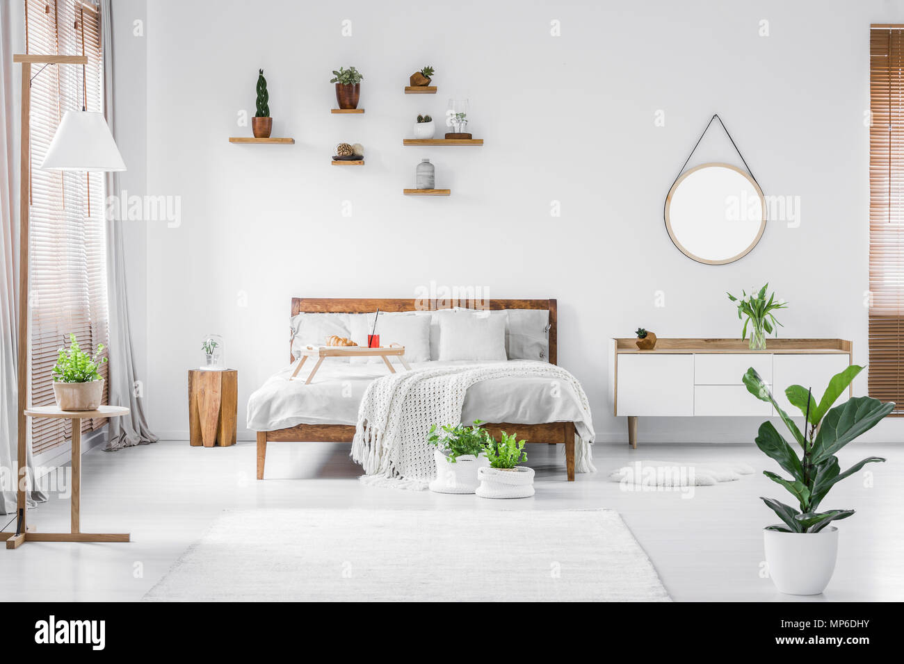 Mattina in una luminosa e soleggiata bianca e moderna camera da letto interni con arredi in legno. Cuscini, coperte e il vassoio per alimenti sul letto, comodino accanto a e h Foto Stock