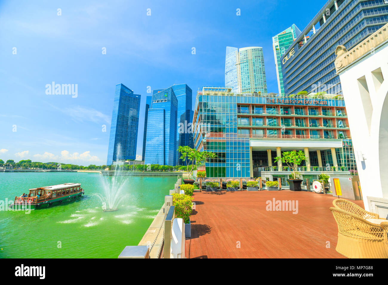 Singapore - Aprile 28, 2018: la splendida vista del Fullerton Bay Hotel a cinque stelle di lusso, grattacieli di Singapore il quartiere degli affari e le imbarcazioni turistiche lungo la baia di Marina lungomare in una giornata di sole e cielo blu. Foto Stock