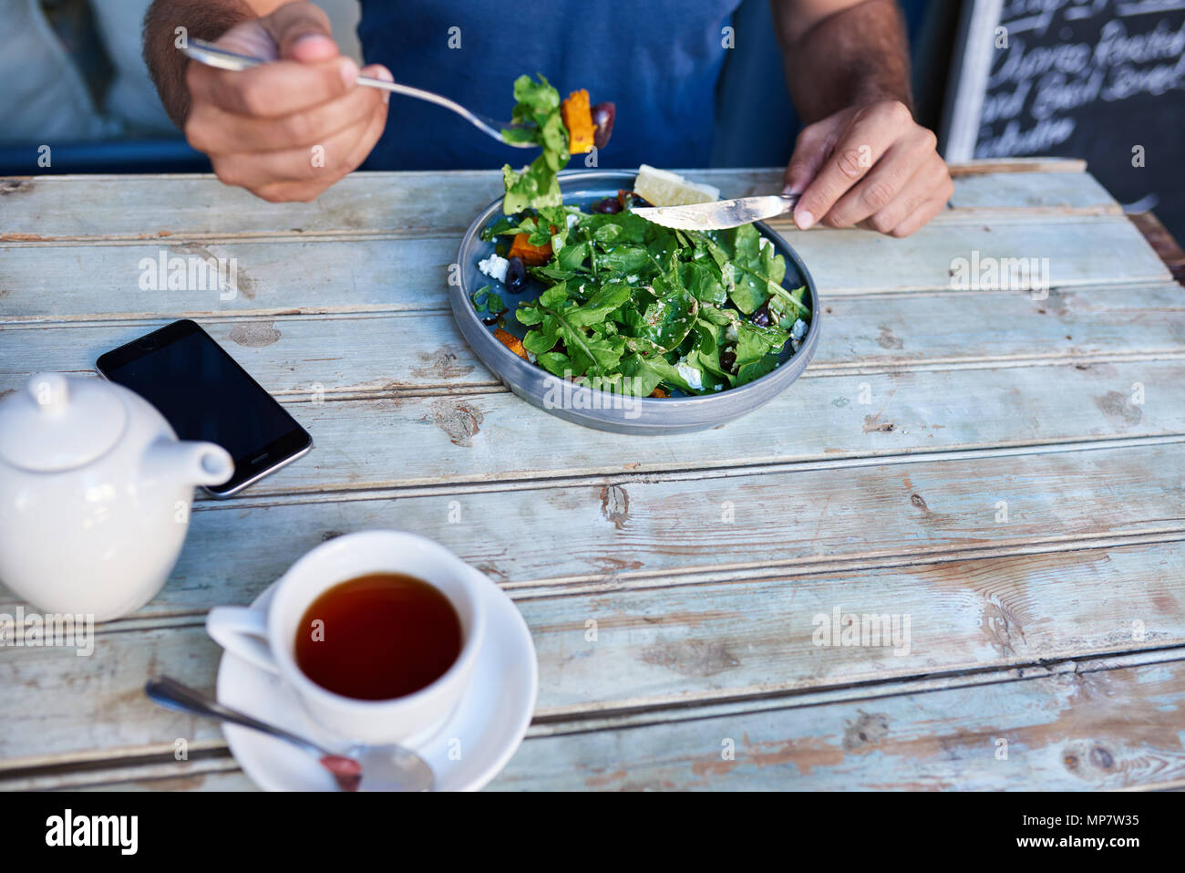 Uomo seduto a tavola in legno rustico mangiare deliziosa insalata Foto Stock