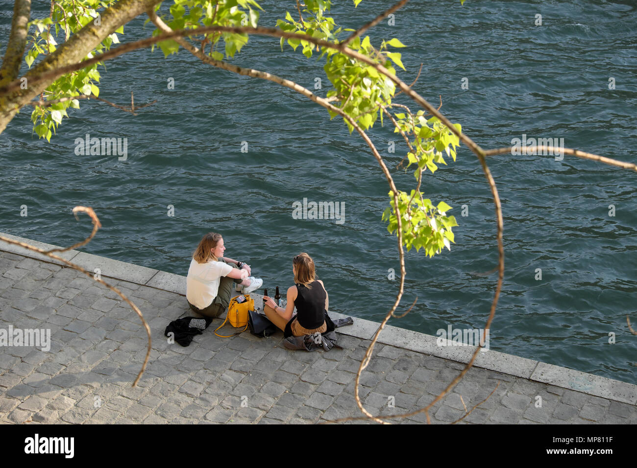 Giovani donne amiche seduti sulla Sponda Sinistra in primavera rilassante con bottiglie di birra dal fiume Senna in sera sunshine Parigi KATHY DEWITT Foto Stock