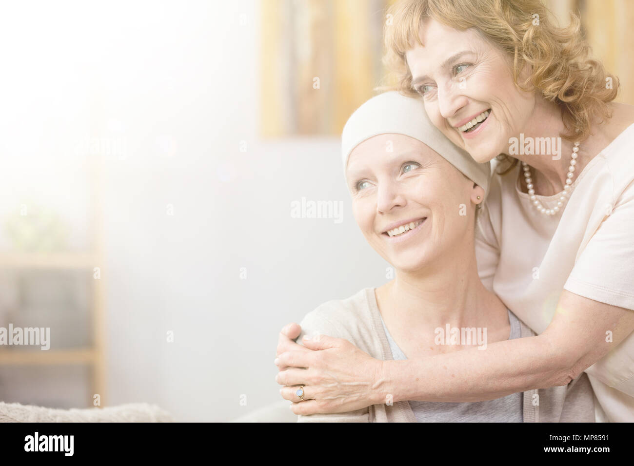 Sorridente donna più anziana che abbraccia il suo amico con il cancro che indossa una sciarpa Foto Stock