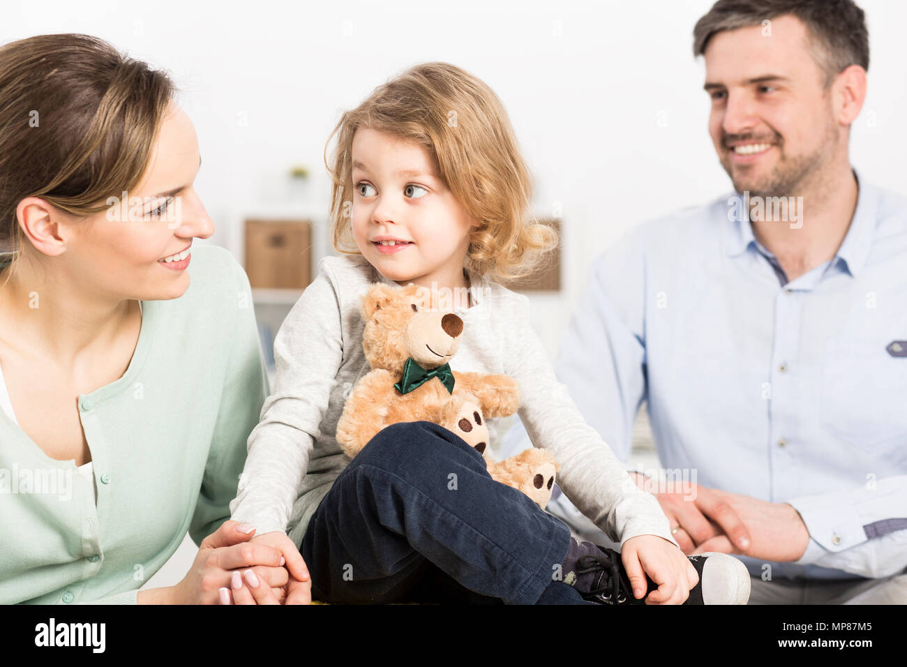La famiglia felice con la madre e la sua piccola figlia tenendo un orsacchiotto in foredground Foto Stock