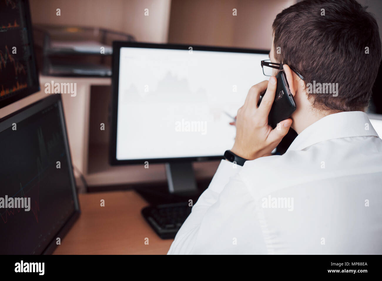 Al di sopra della spalla vista e stock broker trading online mentre ad accettare ordini per telefono. Più schermi di computer ful di grafici e analisi di dati in background Foto Stock