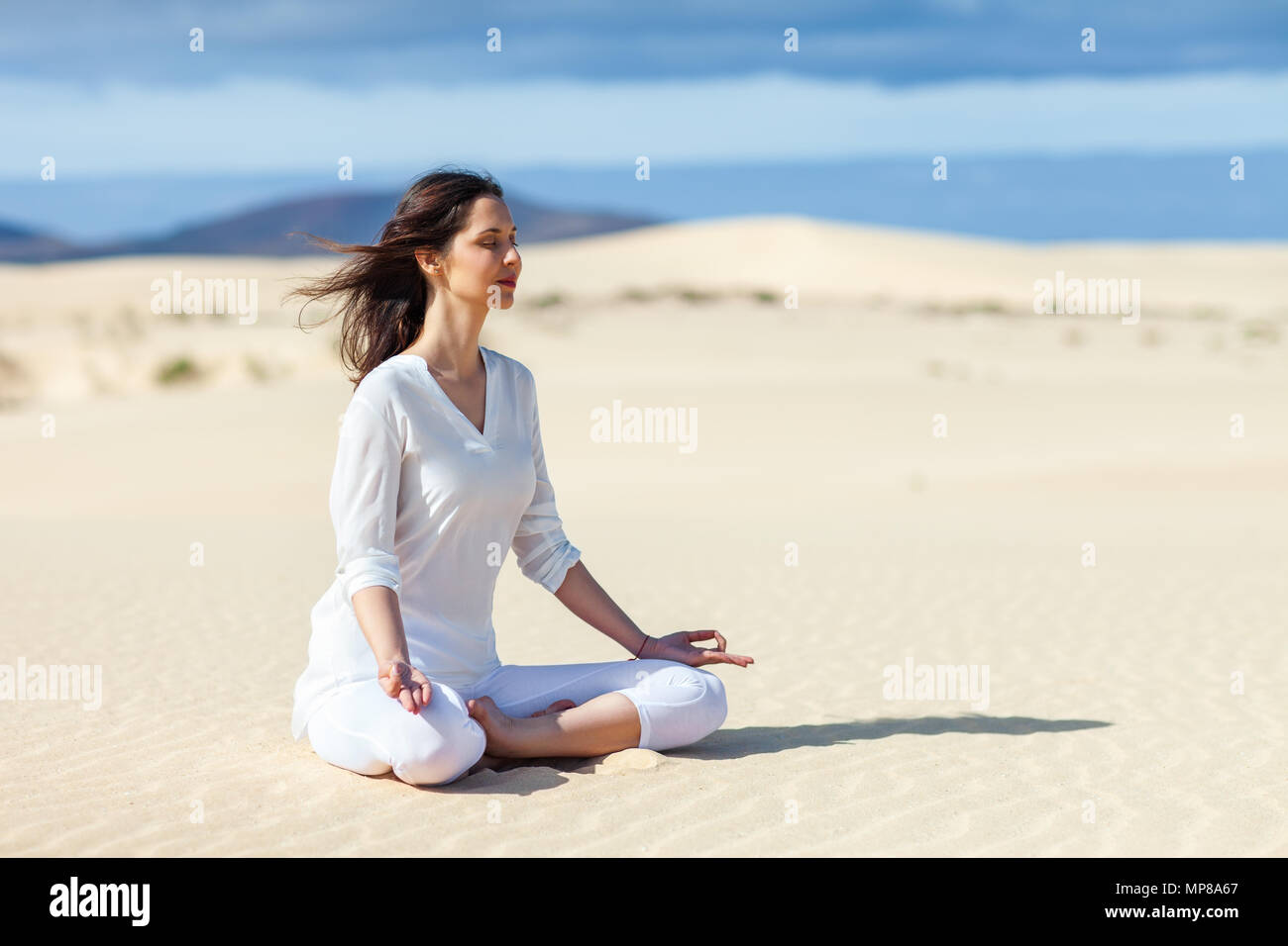 Giovane donna meditando in Lotus pongono nel deserto su Isole Canarie, Spagna. Padmasana. Concetto di relax Foto Stock