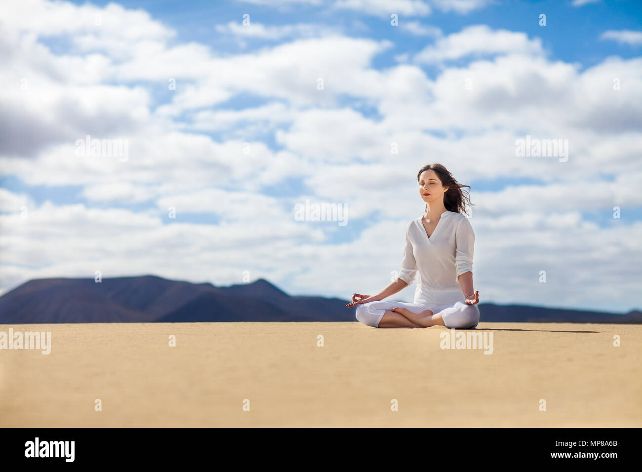 Giovane donna meditando in Lotus pongono nel deserto su Isole Canarie, Spagna. Padmasana. Concetto di relax Foto Stock