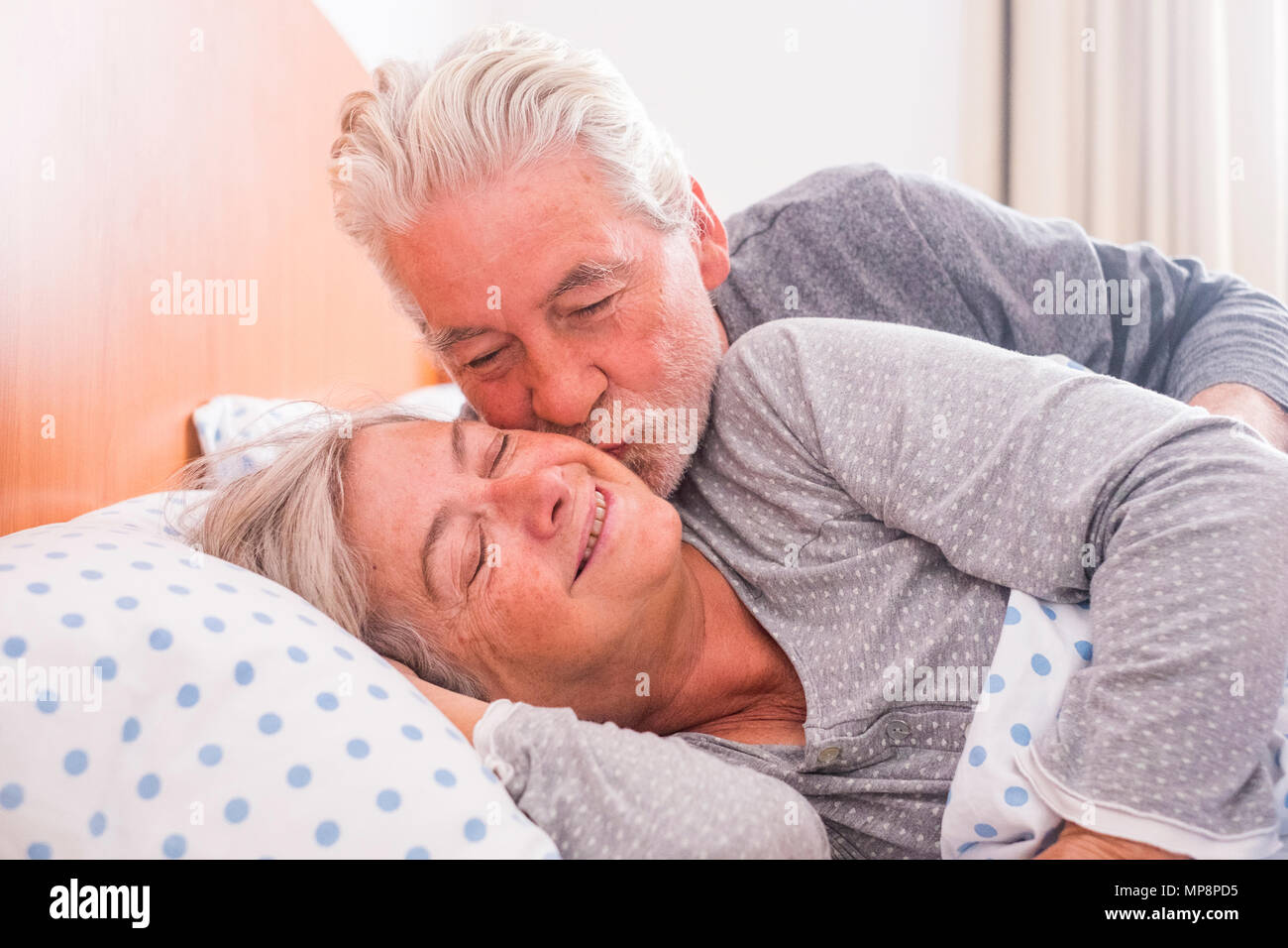 Paio di senior persone sposate riposo a letto, godendo la sveglia con un bacio. Felice pensionato uomo caucasico e donna Foto Stock
