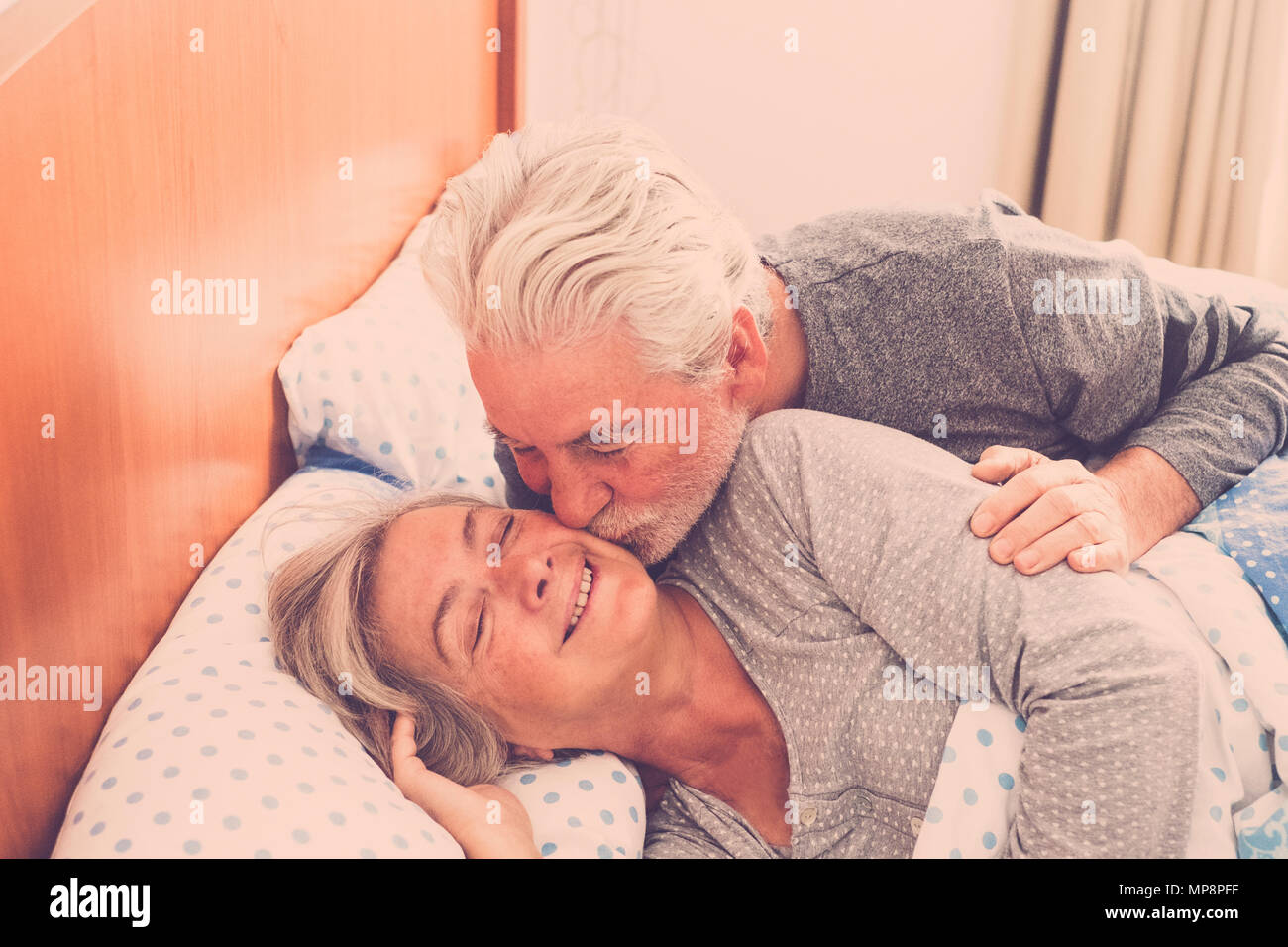 Paio di senior persone sposate riposo a letto, godendo la sveglia con un bacio. Felice pensionato uomo caucasico e donna Foto Stock