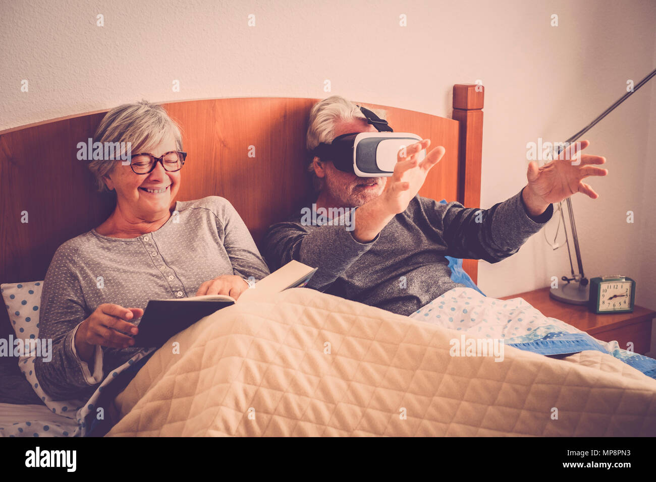 Paio di senior persone sposate riposo a letto, di lettura o di fare nuove esperienze con la realtà virtuale. Felice pensionato uomo caucasico e donna Foto Stock